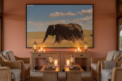 Across the Mara — Lone Elephant fine art print displayed in a luxury safari lodge lounge, terracotta wall, rattan chairs, warm candlelight, no frame — Wild East Visuals