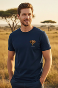 A man stands on the golden African savannah at sunset wearing the Wild East Navy Tee — acacia trees silhouetted behind him, the wild at his back. Wear the Wild. Wild East Visuals.