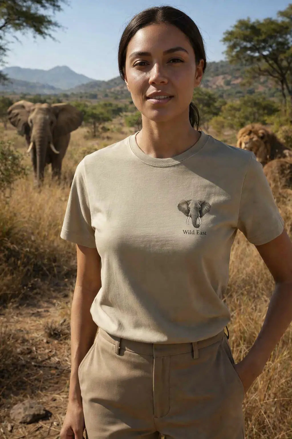 Woman wearing Wild East Sand Tee in the African bush with elephants and lion in background — Wild East Visuals