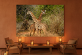 The Crossing — Two Giraffes fine art print displayed in a luxury safari lodge lounge, terracotta wall, rattan chairs, warm candlelight, no frame — Wild East Visuals
